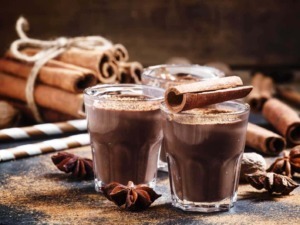 Deliziose cioccolate calde con cannella in bicchieri di vetro, accompagnate da bastoncini di cannella e spezie, perfette per le idee di ricette e dolci autunnali.