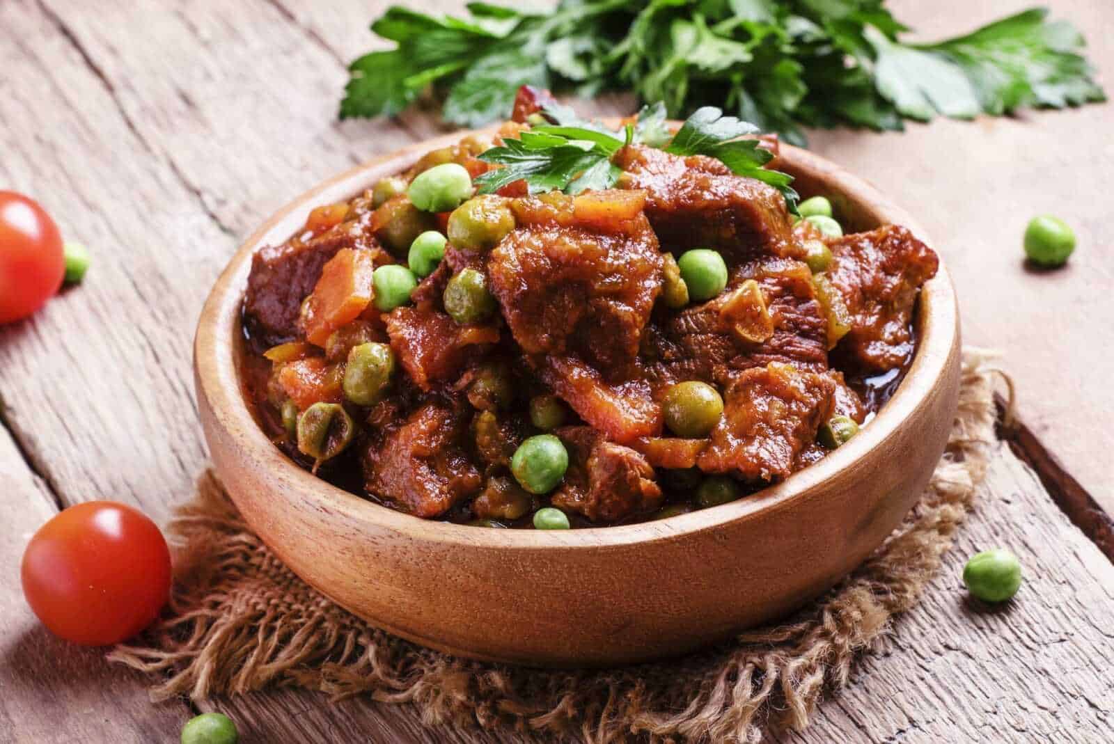 Ricetta di stufato di carne con piselli in ciotola di legno, ingrediente tradizionale italiano, pasto sostanzioso e ricco di sapore, cucina fatta in casa con verdure fresche e carne di qualità.