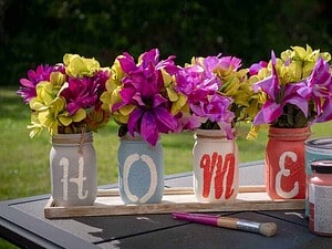 Vasi decorativi con fiori colorati, scritte Personalizzate, tavolo in giardino con vernice, pennello e barattoli di vernice, decorazioni floreali per esterni.