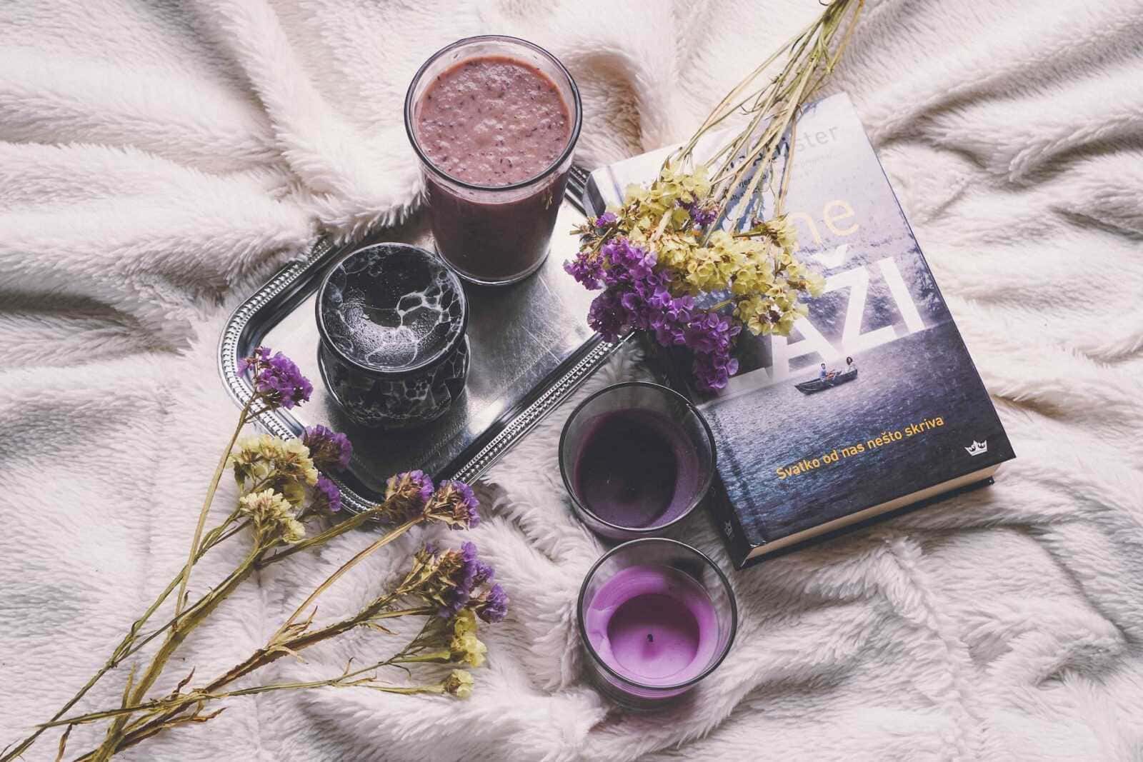 10 progetti fai da te con candele profumate per uno spazio accogliente 6 Un servizio di tocco retrò con bevande colorate, fiori secchi e un libro, tutto disposto su una coperta morbida, creando un ambiente accogliente e rilassante per una pausa di lettura e relax.