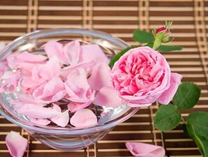 Petali di rosa rosa in una ciotola di vetro con rosa intera e foglie verdi su uno sfondo di bambù.