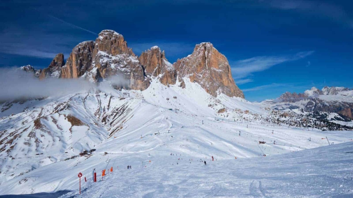 Neve sulle Dolomiti con cime imponenti, cielo blu e piste da sci, scenario panoramico perfetto per gli appassionati di montagna e sport invernali.