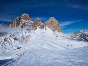 Neve sulle Dolomiti con cime imponenti, cielo blu e piste da sci, scenario panoramico perfetto per gli appassionati di montagna e sport invernali.