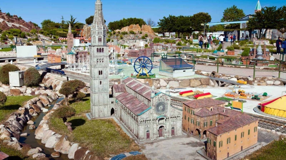 Miniatura di un parco con modelli in miniatura di edifici e attrazioni, tra cui una chiesa e una torre, visitato da persone, con dettagli realistici e ambientazione all'aperto sotto un cielo azzurro.