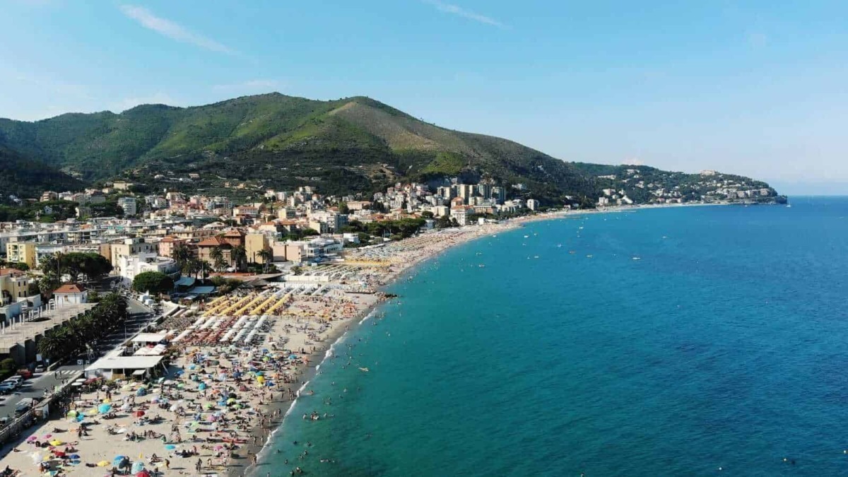 Spiaggia affollata a terracina con ombrelloni colorati e il mare azzurro, sullo sfondo montagne verdeggianti e un cielo sereno, ideale per vacanze al mare e relax estivo.
