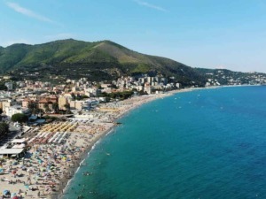 Spiaggia affollata a terracina con ombrelloni colorati e il mare azzurro, sullo sfondo montagne verdeggianti e un cielo sereno, ideale per vacanze al mare e relax estivo.