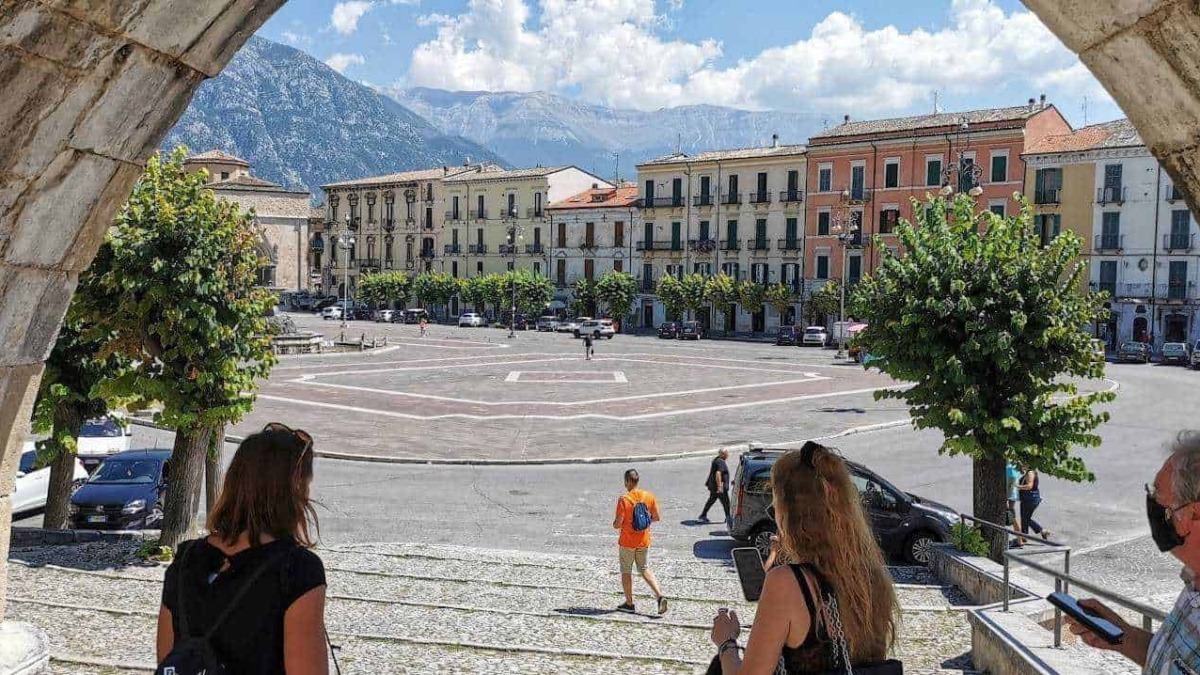 Passeggiata nel centro storico di un paesino italiano con piazza e montagne sullo sfondo, al centro di Appunti Sul Blog.