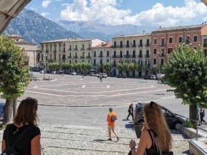Passeggiata nel centro storico di un paesino italiano con piazza e montagne sullo sfondo, al centro di Appunti Sul Blog.