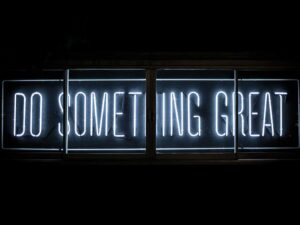 Scritte neon luminose "Do Something Great" su sfondo scuro, messaggio motivazionale in stile urban e motivazionale.