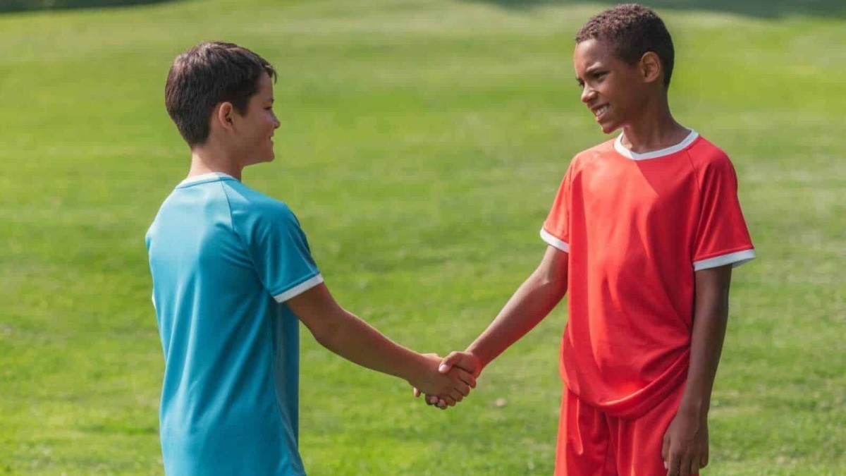 Bambini in divisa sportiva che si stringono la mano sul campo di calcio verde all'aperto.