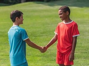 Bambini in divisa sportiva che si stringono la mano sul campo di calcio verde all'aperto.