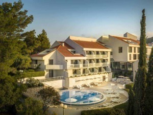 Elegante hotel con piscina all'aperto circondata da alberi e vegetazione, edifici moderni con tetti in terracotta, ideale per vacanze rilassanti in una località turistica italiana.