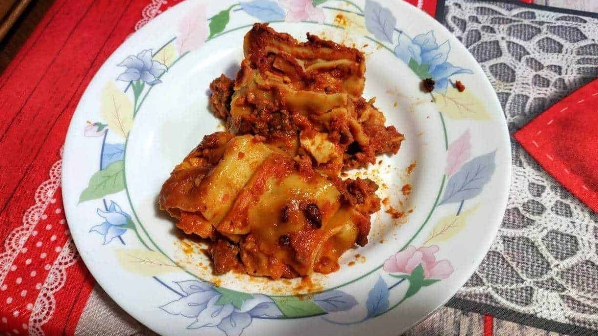 Figli di lasagna fatti in casa con besciamella e pomodoro, serviti in un piatto decorato, su tavolo con tovaglia colorata, deliziose e tradizionali ricette italiane.