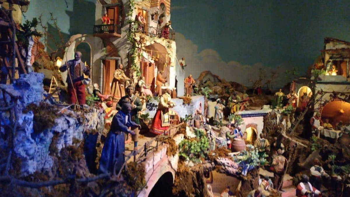 Vicino alle case di un villaggio natalizio con miniature di personaggi e scenari festivi, decorato con luci calde e dettagliis. Perfetto esempio di decorazioni natalizie artigianali e tradizionali.