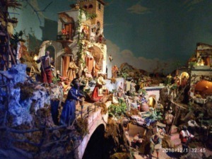 Vicino alle case di un villaggio natalizio con miniature di personaggi e scenari festivi, decorato con luci calde e dettagliis. Perfetto esempio di decorazioni natalizie artigianali e tradizionali.