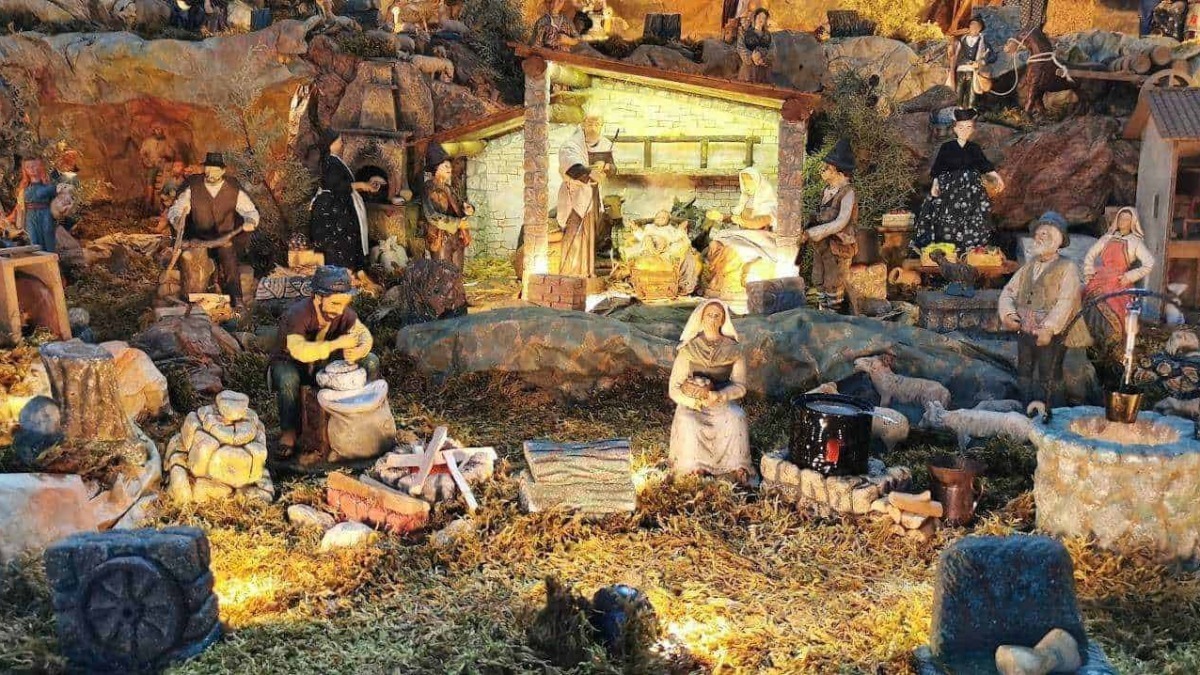 Miniatura del presepe natalizio con statuine di terracotta e luci calde, situato in un paesaggio naturale con rocce e vegetazione, rappresentando scene tradizionali di Natale.