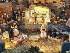 Miniatura del presepe natalizio con statuine di terracotta e luci calde, situato in un paesaggio naturale con rocce e vegetazione, rappresentando scene tradizionali di Natale.