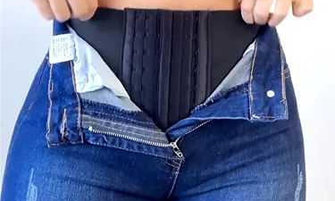 Cintura e jeans aperti, mostra una donna che si sta preparando a indossare un pantalone.