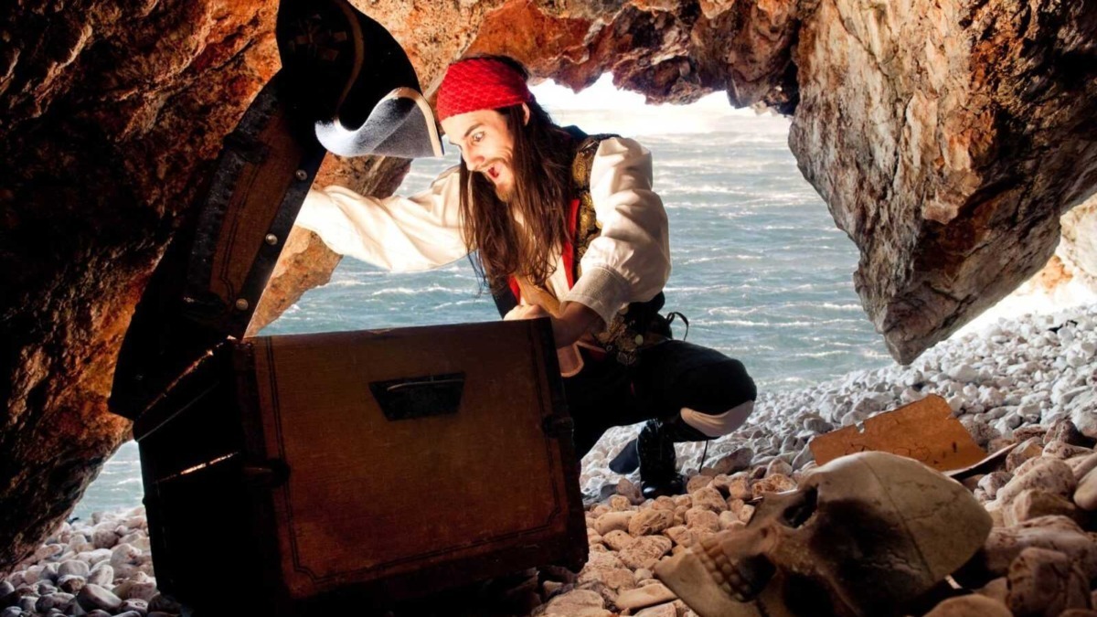 Teschio e scatola di legno in una grotta sulla spiaggia con uomo pirata in costume, avventura piratesca, scoperta segreti nascosti, atmosfera misteriosa e ambiente marino.