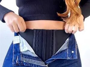 Cintura e jeans aperti, mostra una donna che si sta preparando a indossare un pantalone.