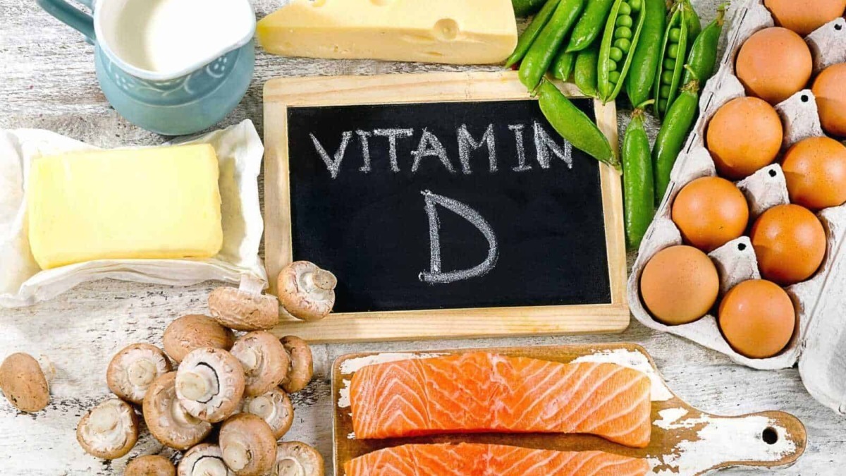 Varianti di alimenti ricchi di vitamina D, tra cui salmone, uova, funghi, latte e verdure verdi, disposti su tavolo in vista di una dieta sana e equilibrata.