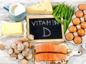 Varianti di alimenti ricchi di vitamina D, tra cui salmone, uova, funghi, latte e verdure verdi, disposti su tavolo in vista di una dieta sana e equilibrata.