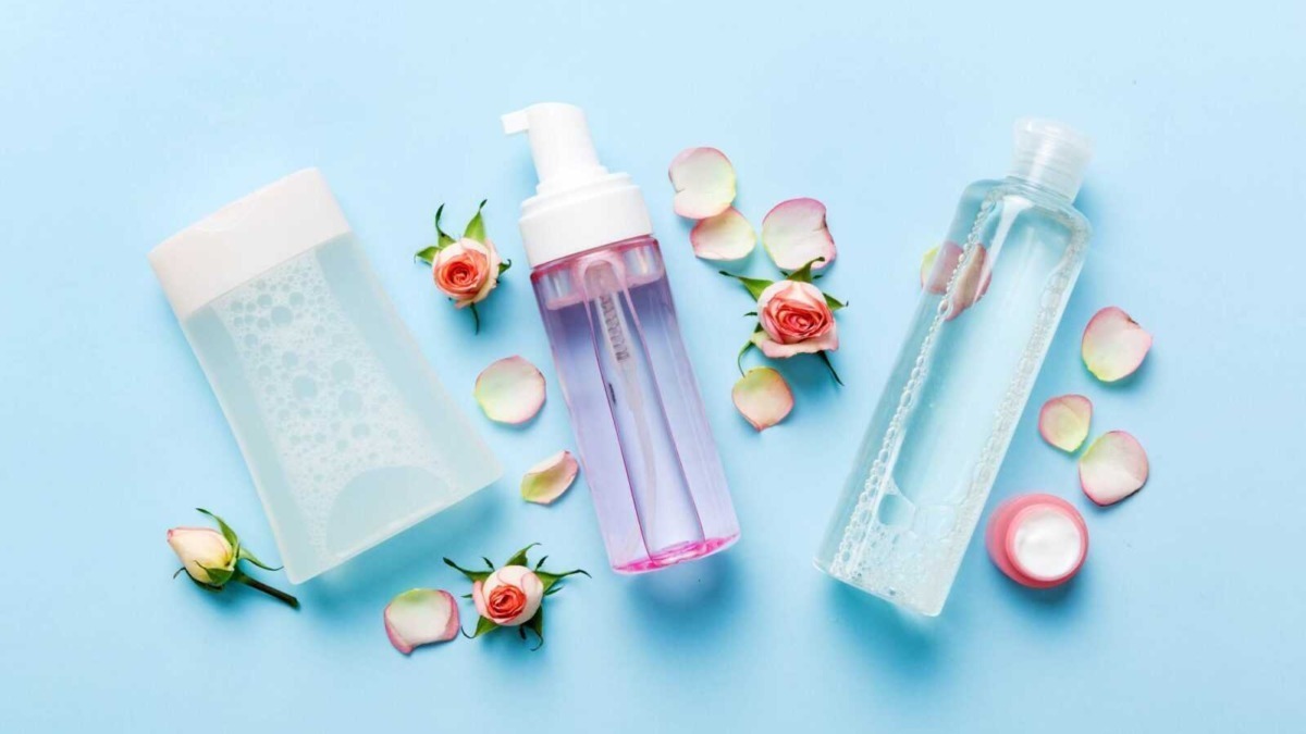 Flaconi di prodotti per la cura della pelle e fiori rosa con petali su sfondo azzurro, simbolo di bellezza, skincare e ingredienti naturali.