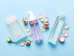 Flaconi di prodotti per la cura della pelle e fiori rosa con petali su sfondo azzurro, simbolo di bellezza, skincare e ingredienti naturali.