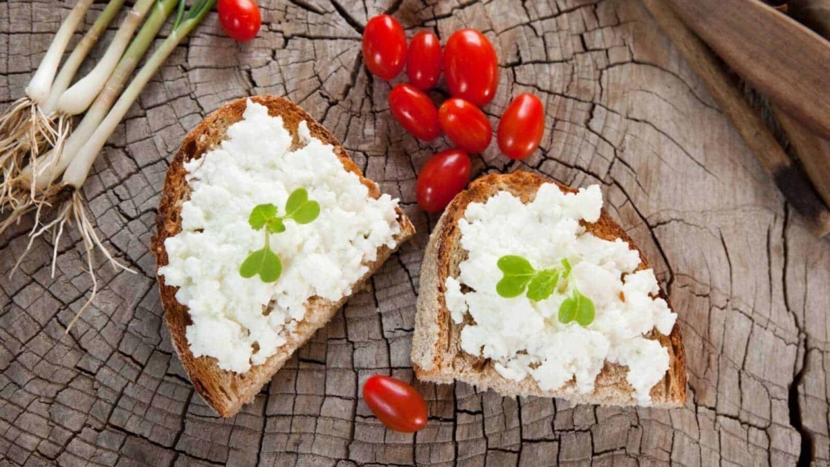 Pane integrale con ricotta, pomodorini e cipollotti su un tagliere di legno come sfondo rustico, perfetto per ricette salutari e alimentazione naturale.