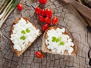 Pane integrale con ricotta, pomodorini e cipollotti su un tagliere di legno come sfondo rustico, perfetto per ricette salutari e alimentazione naturale.