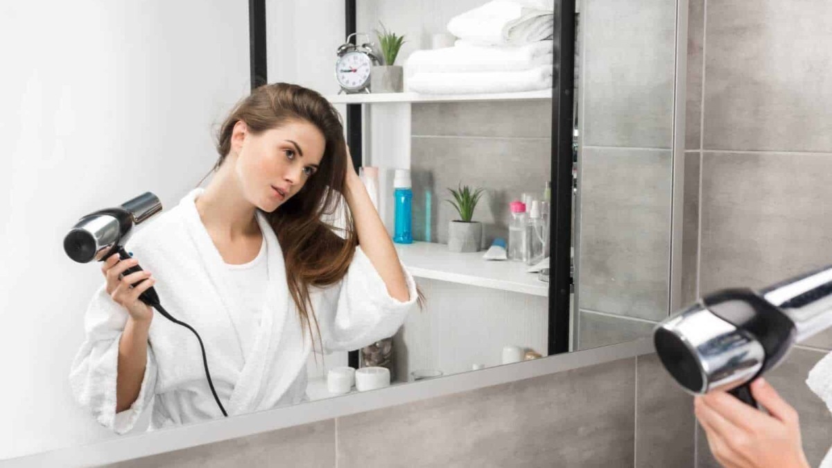 Ragazza che si asciuga i capelli con il phon davanti allo specchio in bagno, cura dei capelli, routine quotidiana di bellezza, ambientazione moderna e minimalista.