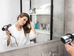 Ragazza che si asciuga i capelli con il phon davanti allo specchio in bagno, cura dei capelli, routine quotidiana di bellezza, ambientazione moderna e minimalista.
