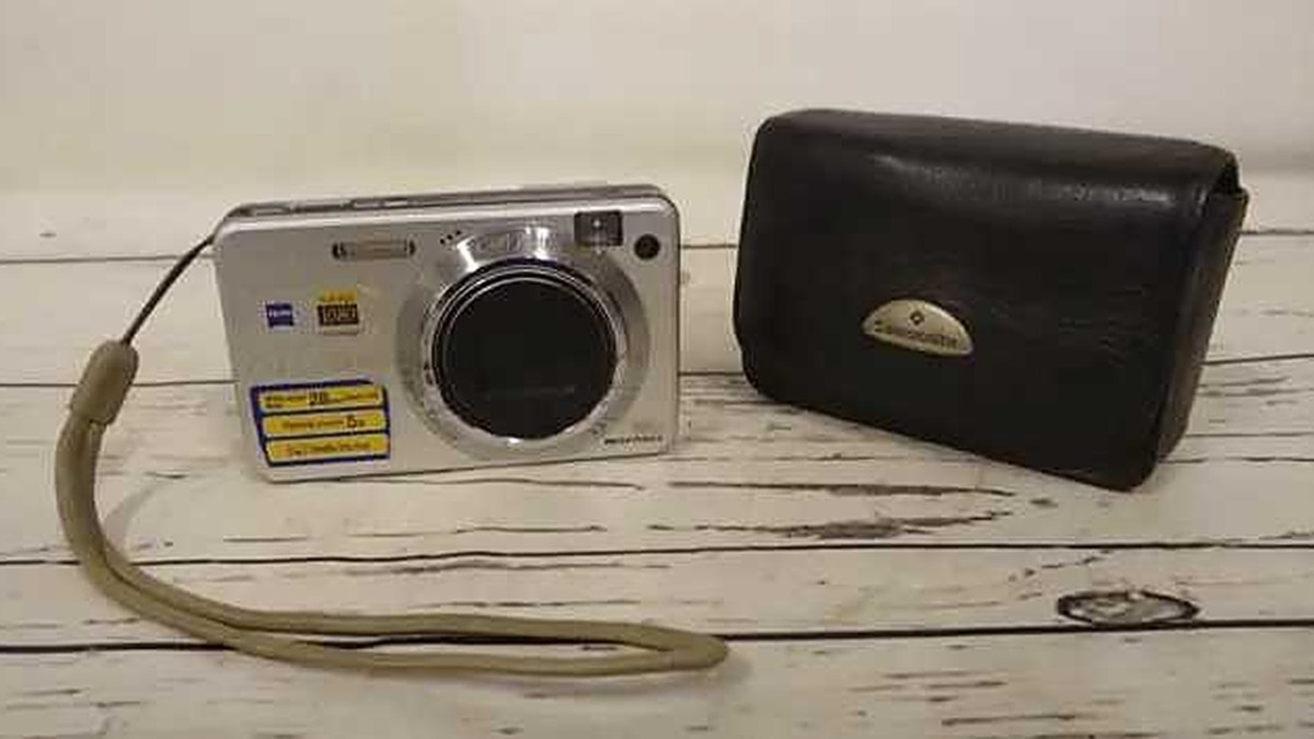 Fotocamera digitale portatile e custodia in pelle su superficie di legno bianco.