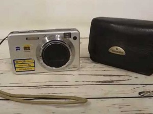 Fotocamera digitale portatile e custodia in pelle su superficie di legno bianco.