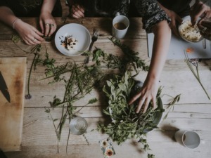 Un gruppo di persone che prepara un'insalata con verdure fresche su un tavolo di legno ricco di ingredienti e utensili da cucina, ambiente conviviale e informale.