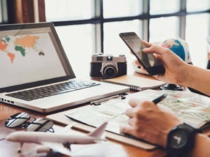 Viaggio e tecnologia: persona che utilizza smartphone e laptop in uno spazio di coworking con mappamondo, macchina fotografica e planning di viaggio.