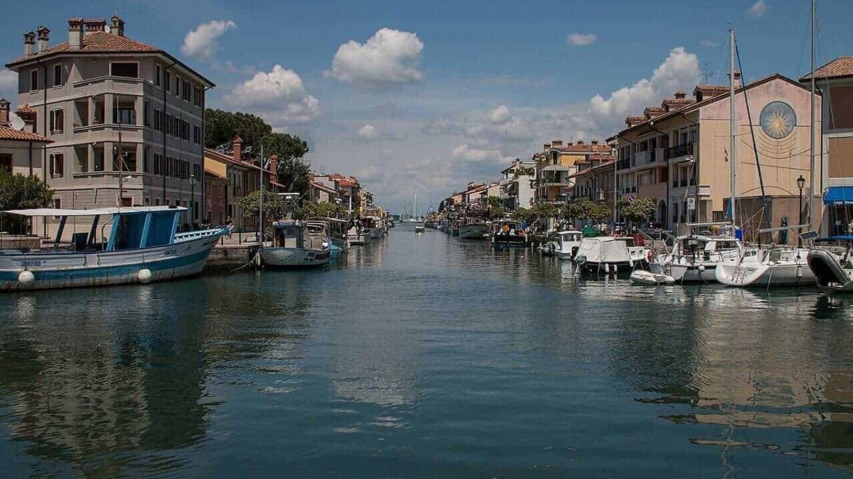 Barche ormeggiate lungo il canale di un porto turistico in una pittoresca zona residenziale, con edifici colorati e un cielo sereno, ideale per immagini di viaggi e turismo nautico.