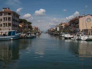 Barche ormeggiate lungo il canale di un porto turistico in una pittoresca zona residenziale, con edifici colorati e un cielo sereno, ideale per immagini di viaggi e turismo nautico.