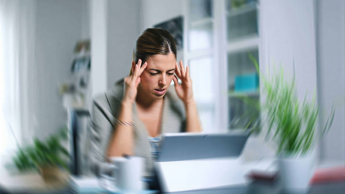Stress da lavoro, donna che si tiene la testa con entrambe le mani mentre guarda il tablet, ambientazione moderna in ufficio.