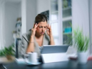 Stress da lavoro, donna che si tiene la testa con entrambe le mani mentre guarda il tablet, ambientazione moderna in ufficio.
