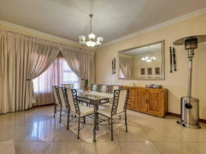 Elegante sala da pranzo con grande tavolo e sedie in stile classico, grandi tende beige e specchio decorativo. Ambiente luminoso e accogliente, perfetto per pranzi familiari e incontri conviviali.