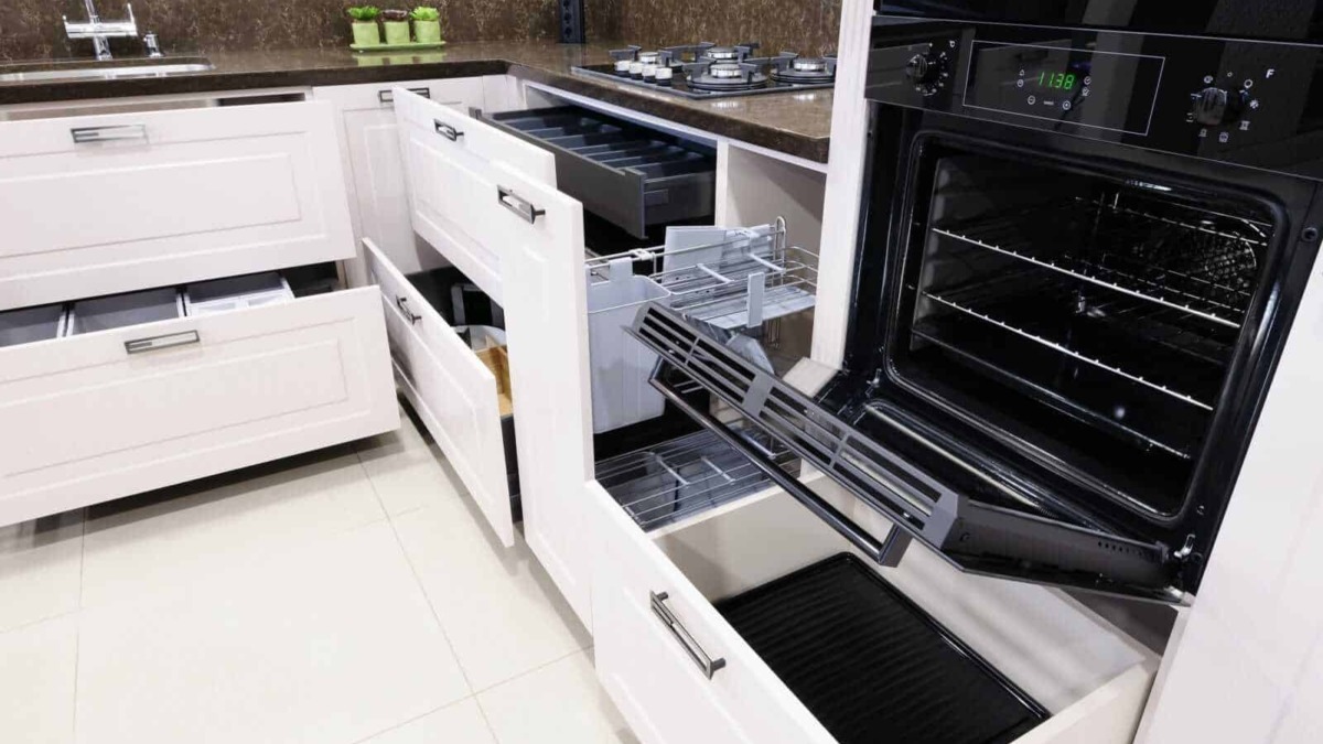 Ripiano cottura a gas e forno elettrico aperto in cucina moderna con mobili bianchi e dettagli neri, vista da vicino.