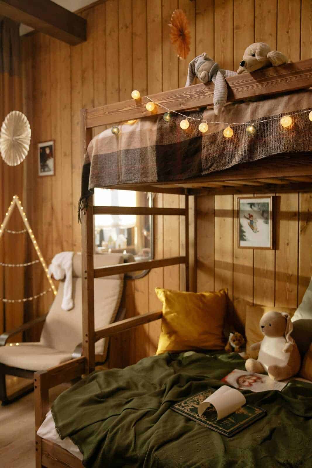 Letto a soppalco in stile rustico decorato con luci di Natale, peluche e tende a quadri, ambientazione accogliente e calda in un chalet di legno, atmosfera di casa e comfort per bambini e adulti.