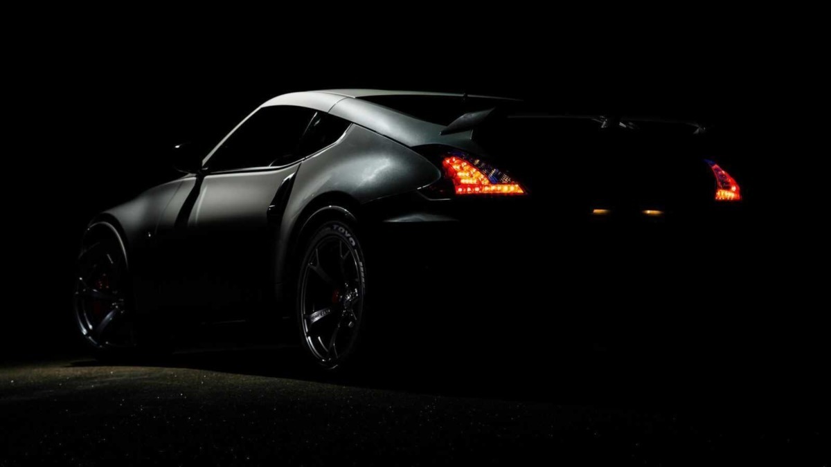 Automobile sportiva nera con luci posteriori illuminate, resa drammatica in ambientazione notturna.