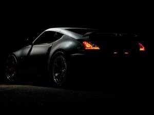 Automobile sportiva nera con luci posteriori illuminate, resa drammatica in ambientazione notturna.