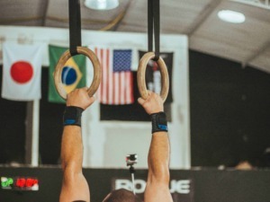 Allenamento di ginnastica con anelli, simbolo di forza e resistenza, scene di fitness e allenamento sportivo in palestra con bandiere internazionali sullo sfondo.