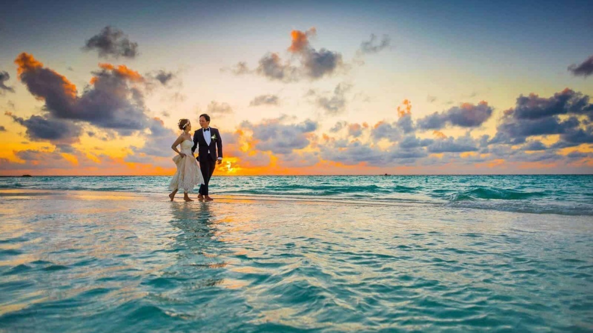 Sposi in abiti da matrimonio sulla spiaggia al tramonto, simbolo di amore e felicità in un matrimonio sulla spiaggia. Perfetta immagine per blog di matrimonio e viaggio romantico.