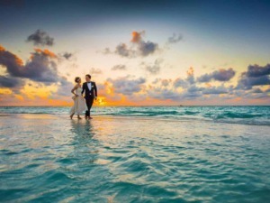 Sposi in abiti da matrimonio sulla spiaggia al tramonto, simbolo di amore e felicità in un matrimonio sulla spiaggia. Perfetta immagine per blog di matrimonio e viaggio romantico.