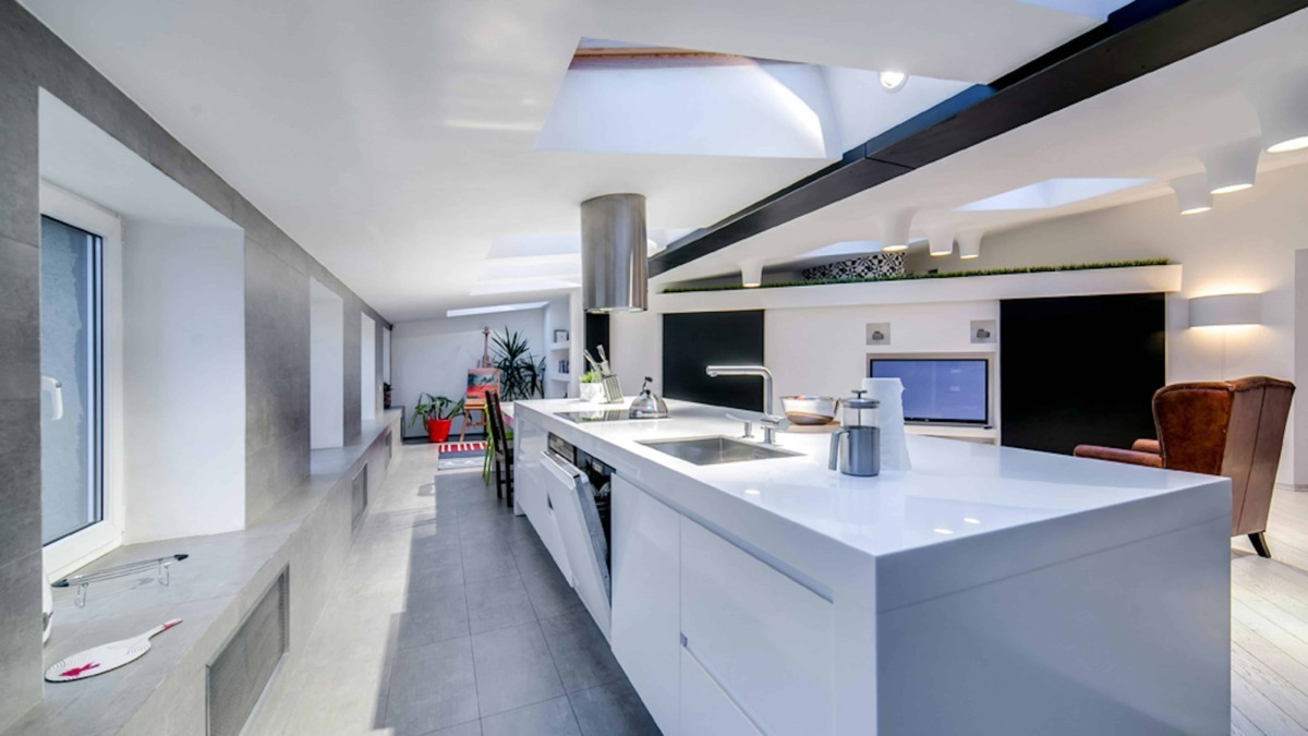 Luminosa cucina moderna con isola centrale, dotata di elettrodomestici innovativi, soffitti con lucernari e design minimalista, ideale per spazi di Living chic a Milano.