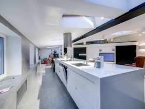 Luminosa cucina moderna con isola centrale, dotata di elettrodomestici innovativi, soffitti con lucernari e design minimalista, ideale per spazi di Living chic a Milano.